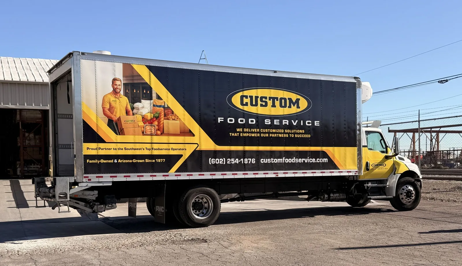 A Custom Food Service delivery truck, branded in yellow and charcoal, parked at the Phoenix warehouse
